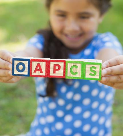 6 year old Latino girl holding 5 blocks that spell out OAPCS